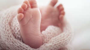 Soft newborn baby feet against a pink blanket.