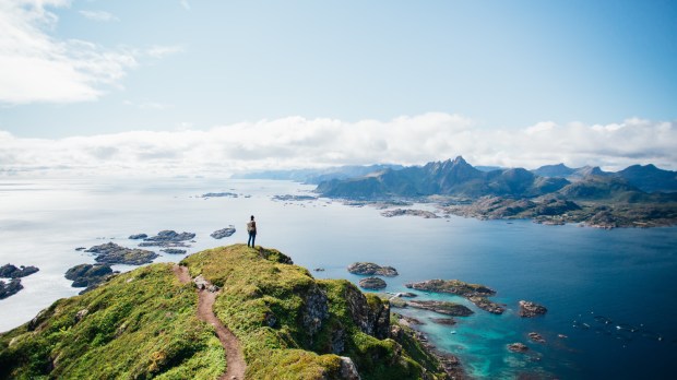 Mężczyzna stojący na szczycie pagórka patrzy na piękny widok zatoki gdzieś w Norwegii.