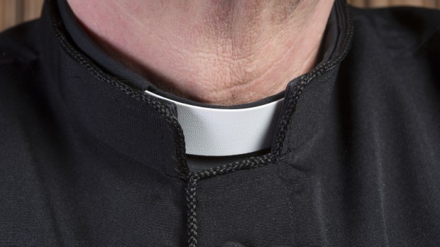 Closeup of the neck of a priest wearing a black shirt with cassock and white clerical collar
