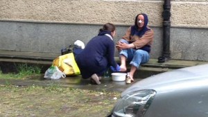 Kobieta myje nogi bezdomnemu na ulicy
