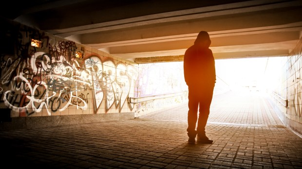 mężczyzna ubrany w bluzę z kapturem stoi samotnie w przejściu podziemnym ze ścianami wymalowanymi graffiti