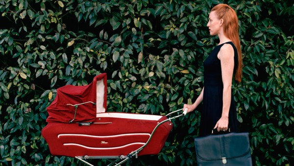 Bizneswoman idąca z teczką pcha przed sobą wózek z dzieckiem