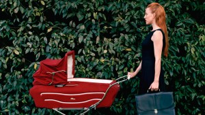 Bizneswoman idąca z teczką pcha przed sobą wózek z dzieckiem