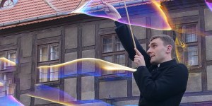 Ksiądz, który opowiada ludziom o Bogu przy puszczaniu baniek mydlanych