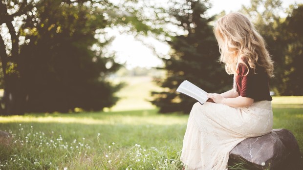 Kobieta siedząca w ogrodzie czyta Pismo Święte