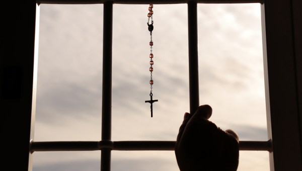 Religious rosary hanging on window with grate