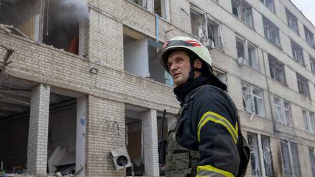 firefighter in front of a residential building destroyed by shelling