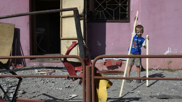 chłopiec bawi się przed swoim domem zniszczonym w nocnym bombardowaniu, Ukraina