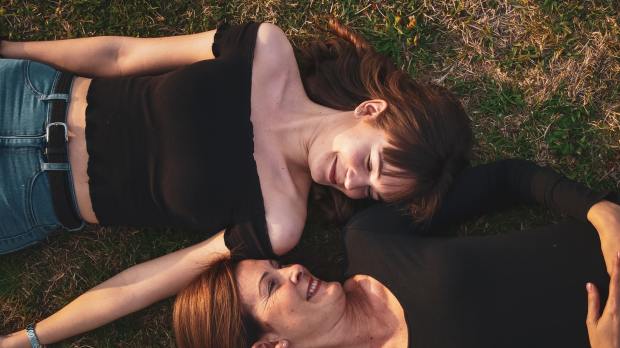 uśmiechnięte mama z nastoletnią córką leżą na trawie i patrzą w swoją stronę