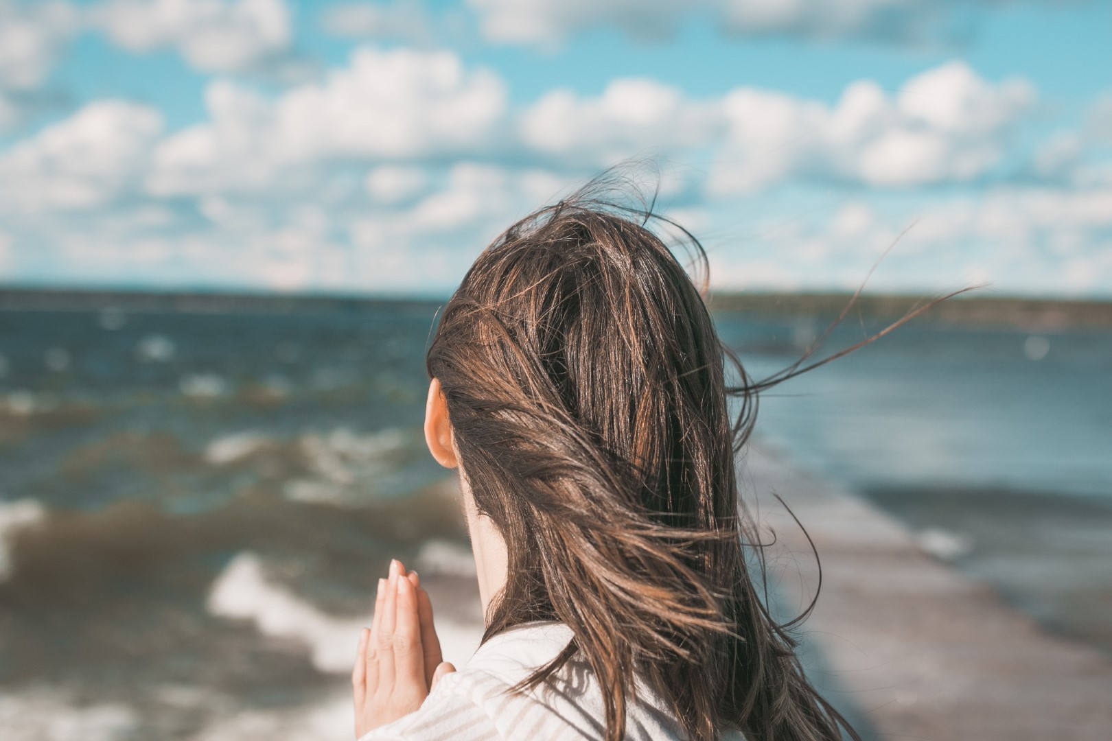 kobieta modli się na plaży, zwrócona w stronę morza