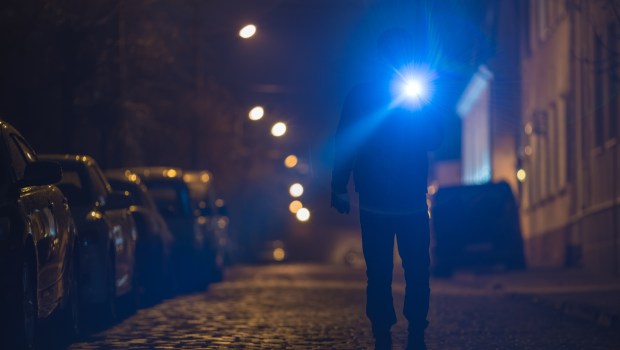 Mężczyzna z latarką idzie ciemną uliczką małego europejskiego miasteczka