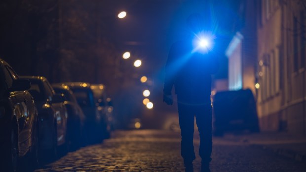Mężczyzna z latarką idzie ciemną uliczką małego europejskiego miasteczka