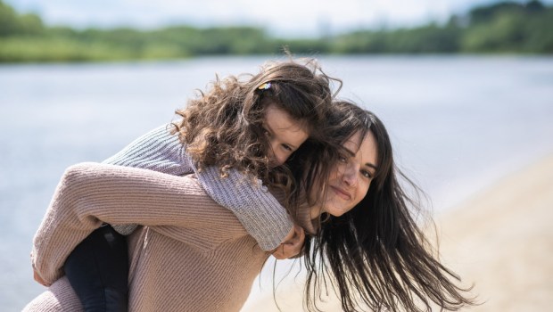matka z córką przytulają się, spacerują po plaży nad brzegiem jeziora