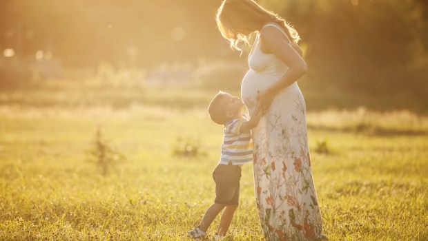 Mały chłopiec obejmuje brzuch mamy w ciąży na świeżym powietrzu