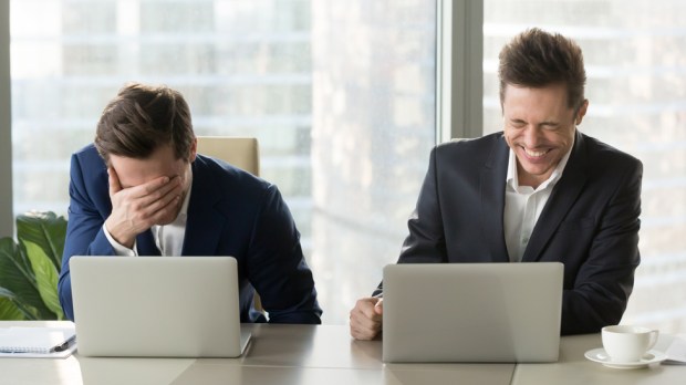 dwóch biznesmenów śmieje się z tego, co widzą na ekranach laptopów