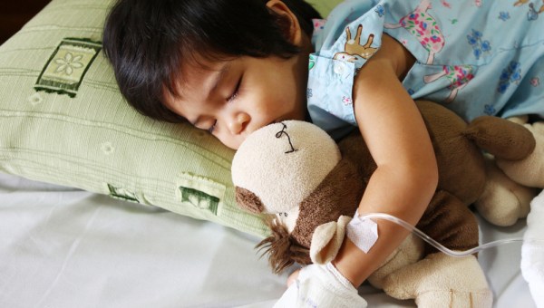 chory chłopiec leży w łóżku i przytula misia