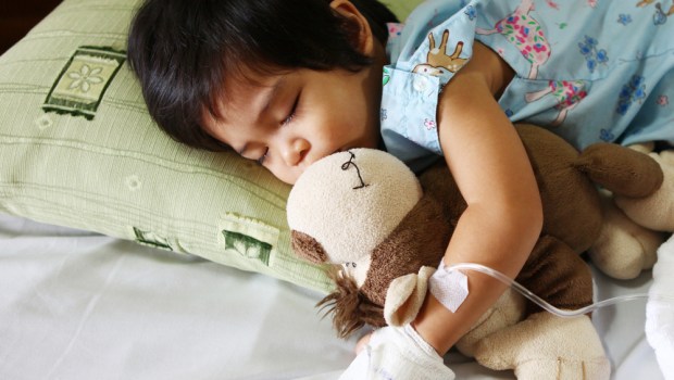 chory chłopiec leży w łóżku i przytula misia