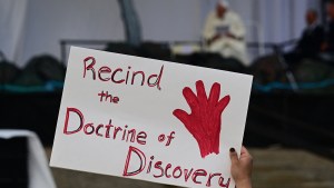 A-person-holds-a-protest-sign-reading-Recind-the-Doctrine-of-Discovery-at-Nakasuk-Elementary-School-Square-in-Iqaluit-AFP
