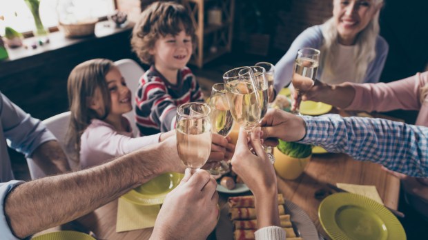 Rodzina wznosi toast siedząc przy stole razem z dziećmi