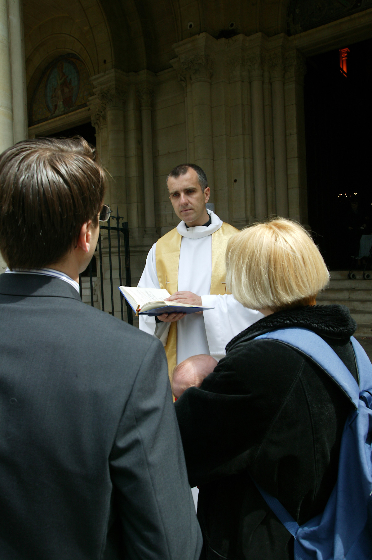 ksiądz rozmawia przed kościołem z rodzicami małego dziecka