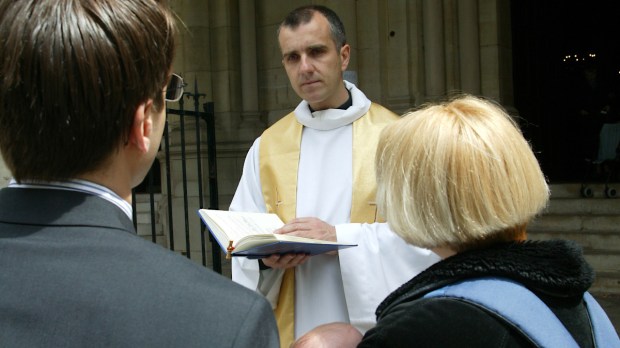 ksiądz rozmawia przed kościołem z rodzicami małego dziecka