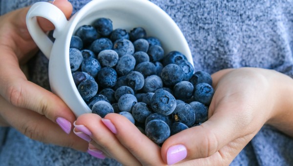 Kobiece dłonie wysypujące z filiżanki jagody