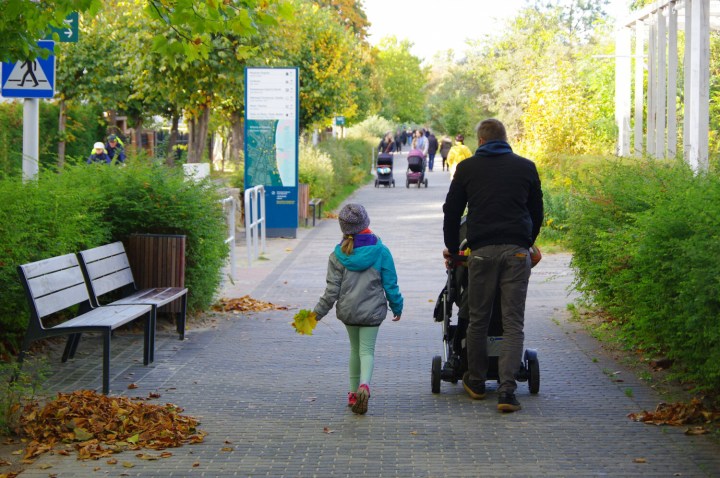 ojciec spaceruje po parku z córką i małym dzieckiem w wózku