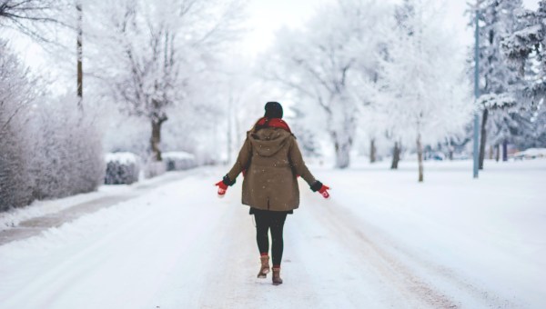 kobieta odwrócona plecami stoi na zaśnieżonej ulicy i rozkłada ręce