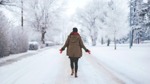 kobieta odwrócona plecami stoi na zaśnieżonej ulicy i rozkłada ręce