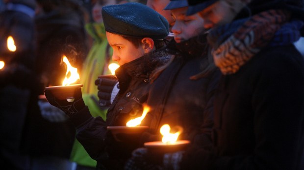 harcerze trzymają w dłoniach zapalone znicze w zimny wieczór na cmentarzu