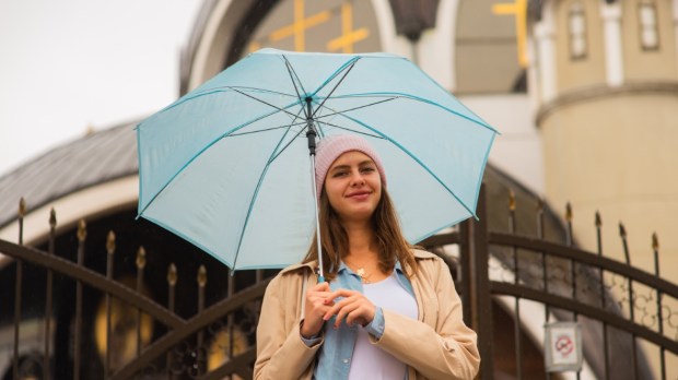uśmiechnięta kobieta stoi przed kościołem i trzyma nad głową niebieski parasol