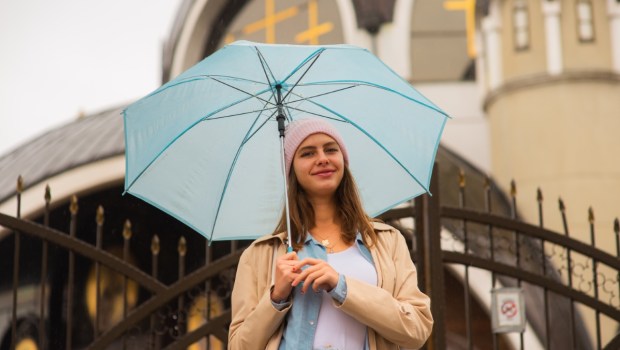 uśmiechnięta kobieta stoi przed kościołem i trzyma nad głową niebieski parasol