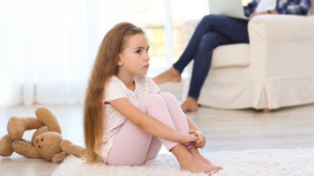 dziewczynka czuje się samotna i siedzi na dywanie gdy jej mama rozmawia przez telefon