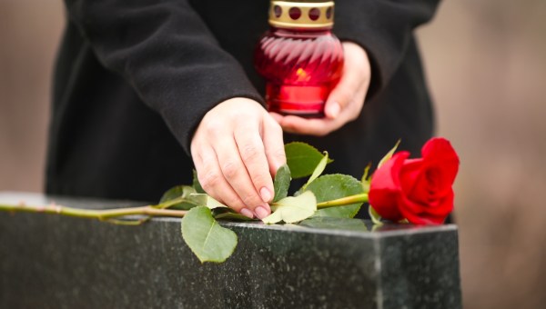 kobieta kładzie różę na nagrobku i trzyma w dłoni zapalony znicz