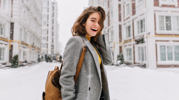 dziewczyna uśmiecha się stojąc na zaśnieżonej ulicy wielkiego miasta