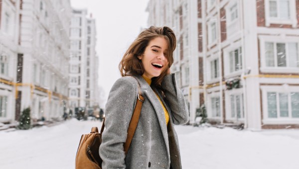 dziewczyna uśmiecha się stojąc na zaśnieżonej ulicy wielkiego miasta