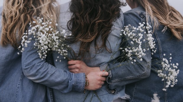 trzy przyjaciółki idą razem przytulone do siebie i trzymają w rękach białe kwiaty