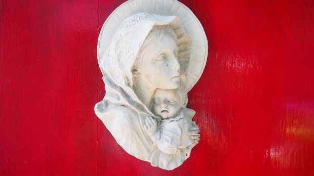 Płaskorzeźba na czerwonej drewnianej ścianie przedstawiająca popiersie Maryi z małym Jezusem