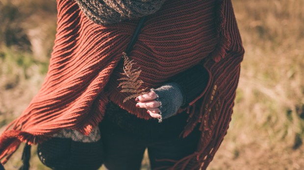 kobieta spaceruje w plenerze trzymając w ręce suchy liść paproci