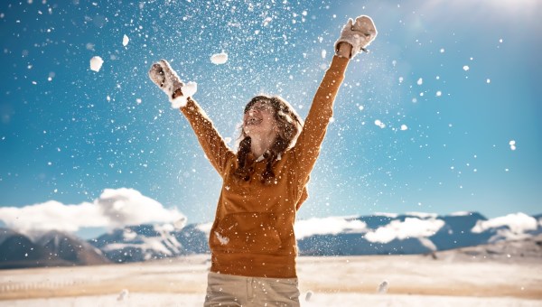 Rozradowana kobieta w wysokich górach podrzuca do góry śnieg