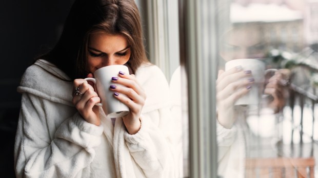 piękna dziewczyna pije kawę z kubka stojąc przy oknie w trakcie zimowego poranka