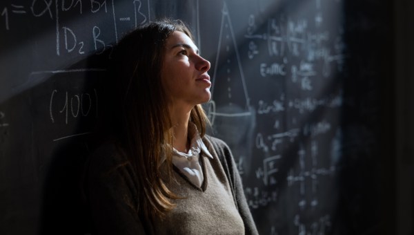 Zamyślona studentka matematyki przed tablicą zapisaną wzorami matematycznymi i fizycznymi