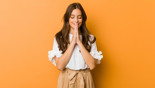 uśmiechnięta młoda dziewczyna modli się ze złożonymi rękami