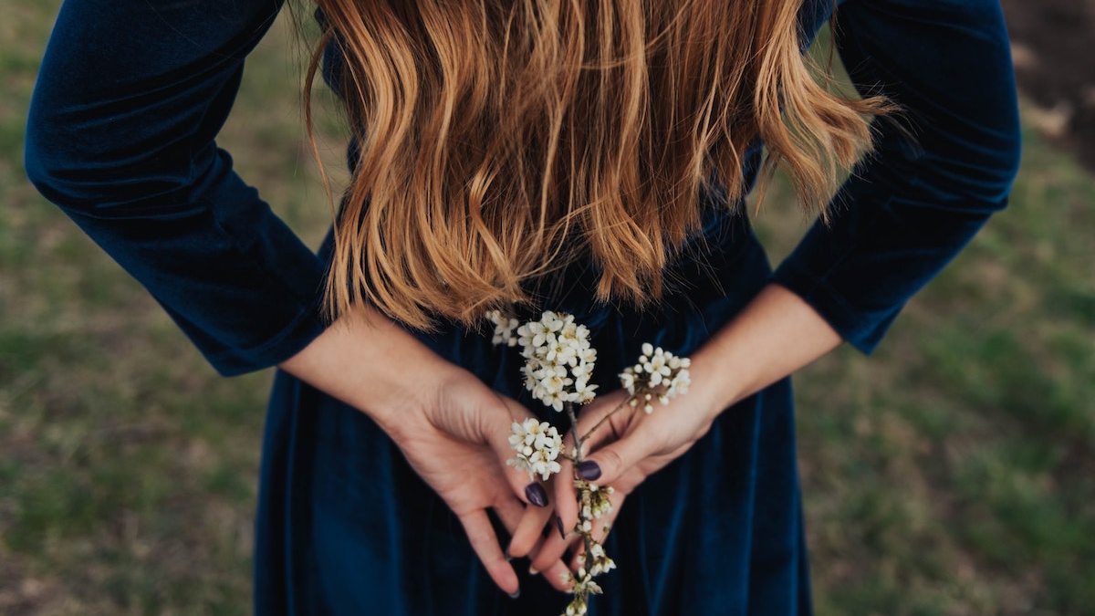 A woman in a navy blue dress holds a flowering twig in her hands