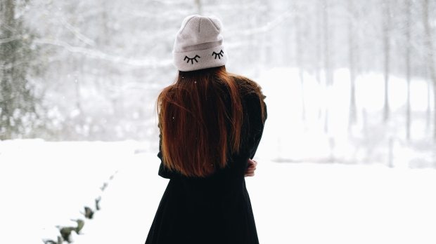 a girl in a gray cap stands with her back turned in a snowy landscape