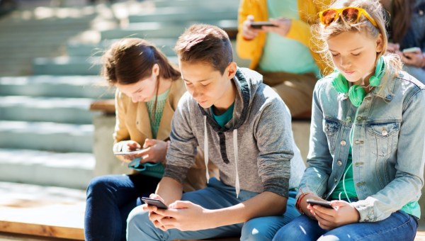 grupa nastolatków siedzi na schodach i wpatruje się w smartfony