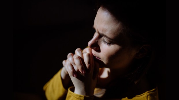 Smutna kobieta błaga Boga o pomoc podczas modlitwy w ciemnym miejscu