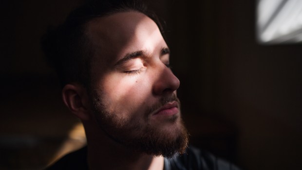 mężczyzna nadstawia drugi policzek w świetle promieni słonecznych przebijających z okna