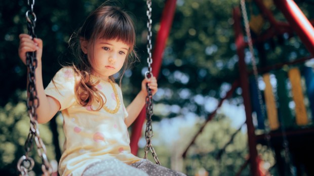dziewczynka bawi się sama na huśtawce na placu zabaw i czuje się samotnie