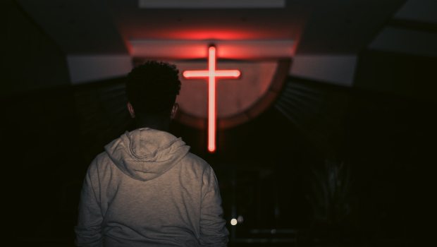 young man looks at red neon cross